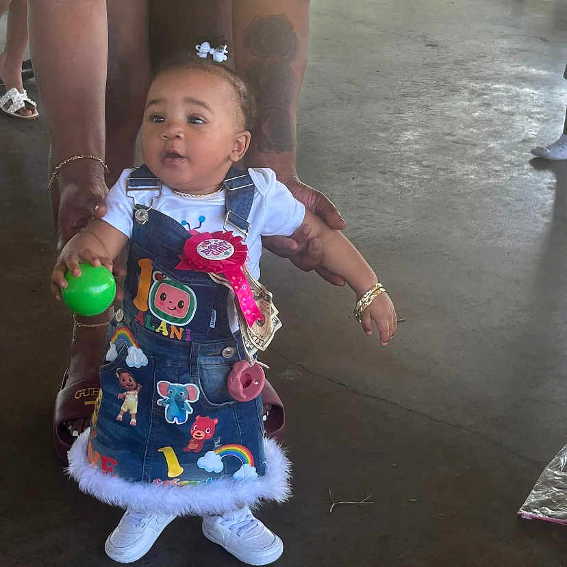 Alani joined the competition — help win amazing prizes! adult_hands, ball, birthday_ribbon, bracelet, casual, celebration, child, colorful_clothing, concrete_floor, cute, denim_dress, hair_bow, helping_hand, indoor, person, playful, standing, tattoo, toddler, white_shoes