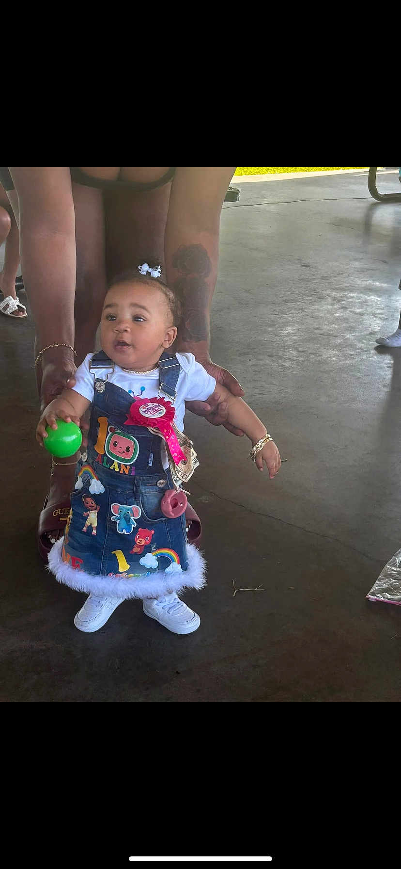Alani joined the competition — help win amazing prizes! toddler, child, denim_dress, ball, tattoo, bracelet, birthday_ribbon, white_shoes, indoor, concrete_floor, adult_hands, cute, colorful_clothing, standing, helping_hand, hair_bow, playful, person, celebration, casual