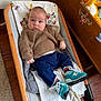 baby, infant, child, sweater, pants, socks, sneakers, baby_rocker, wooden_floor, toy_chest, stuffed_animal, blanket, indoor, floor, furniture, person, cute, cozy, childrens_room, smiling