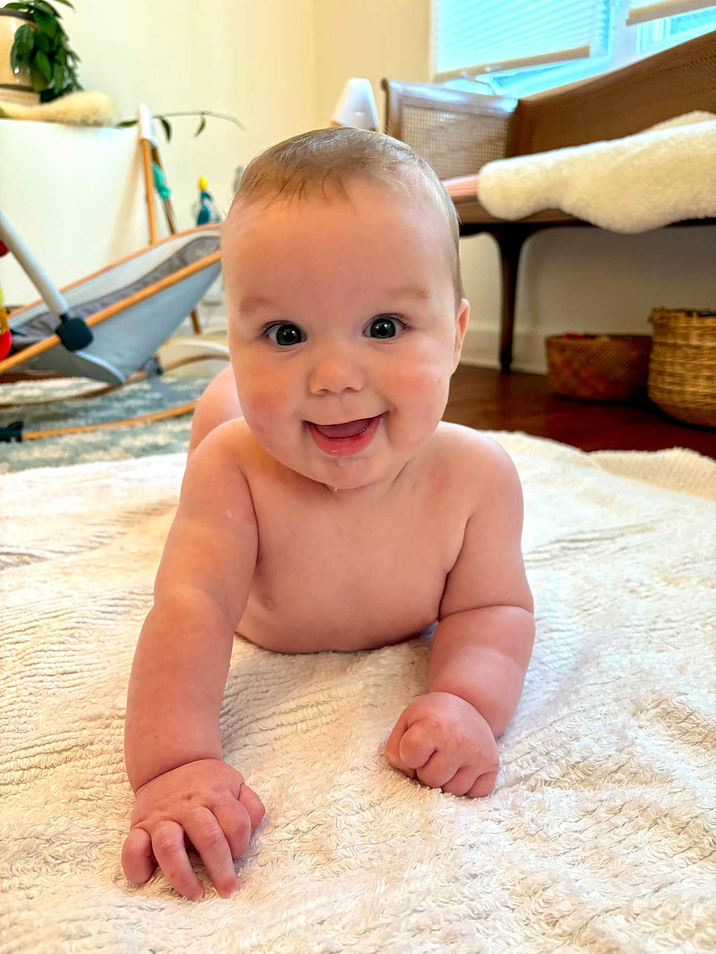 Sonny is registered to the contest to win money with this photo: baby, smiling, tummy, blanket, indoor, living_room, natural_light, face, happy, child, cute, drool, skin, furniture, floor, window, basket, plant, cozy, home