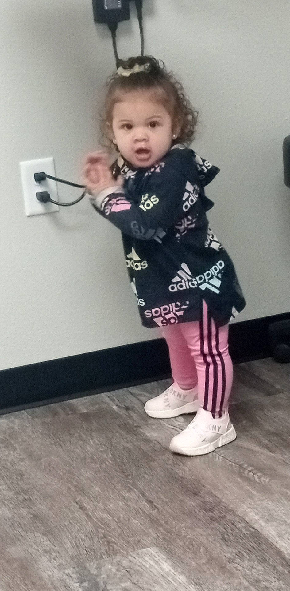 Naomi is registered to the contest to win money with this photo: baby_toddler_clothing, cheek, child, face, floor, flooring, hair, head, human_leg, iris, knee, magenta, pattern, person, sleeve, sock, standing, t_shirt, toddler, white