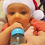 baby, child, santa_hat, bottle, hand, cute, indoor, person, holiday, festive, red_clothing, face, young_child, portrait, feeding, closeup, warm_lighting, holiday_season, infant, holding