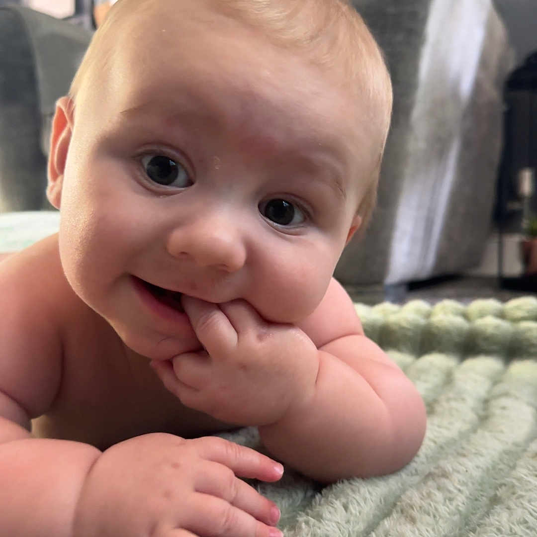 Noah joined the competition — help win amazing prizes! baby, blanket, blurred_background, child, close_up, curious, cute, expression, face, fingers, furniture, hand, indoor, infant, living_room, portrait, skin, smile, soft_lighting, texture