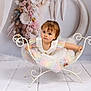 toddler, child, dress, pastel_colors, flower_arrangement, white_chair, wrought_iron, indoor, portrait, cute, baby, floor, decor, moon, curious, sitting, studio, soft_lighting, young_child, playful