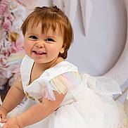 Ninon participe au concours pour gagner de l'argent avec cette photo : toddler, child, smile, white_dress, pastel_colors, tulle, wrought_iron, chair, portrait, flower_background, crescent_moon, indoor, cute, happy, baby, face, skin, short_hair, playful, studio