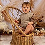toddler, child, wicker_chair, pampas_grass, neutral_colors, indoor, portrait, cute, baby, sitting, cozy, plaid, knitted_vest, floor, decor, basket, soft_lighting, curious, face, person