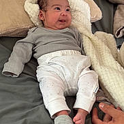Kendall joined the competition — help win amazing prizes! baby, infant, smiling, bed, blanket, clothing, gray_top, white_pants, sock, hand, cozy, soft, cute, lying_down, indoor, person, small_foot, happy, face, expression