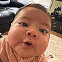 Daleyza is registered to the contest to win money with this photo: baby, child, close_up, face, expression, pink_clothing, ribbed_fabric, living_room, couch, window, blinds, television, furniture, curly_hair, indoor, person, cute, portrait, young_child, cozy