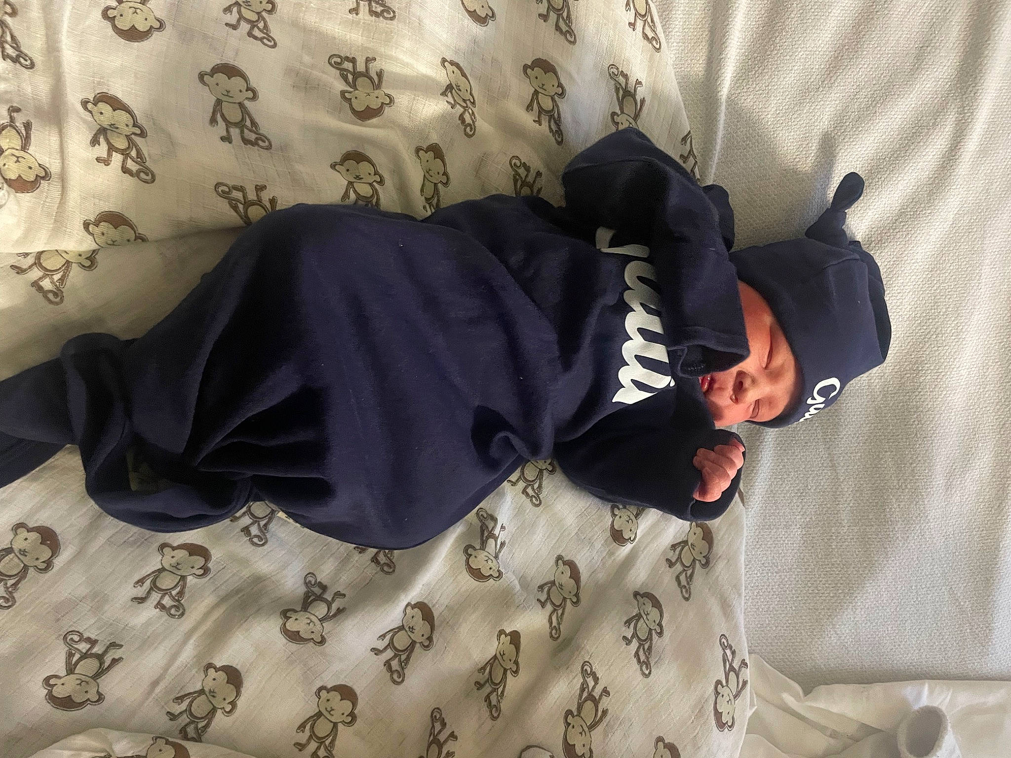 Gatlin is registered to the contest to win money with this photo: bed_sheet, bedding, bedroom, comfort, floor, flooring, fun, glasses, grey, headwear, human_leg, knee, leg, linens, outerwear, pattern, person, room, sitting, sleeve