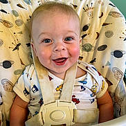 Oliver is registered to the contest to win money with this photo: baby, high_chair, smile, blue_eyes, safety_strap, onesie, patterned_clothing, indoor, child, face, seat, happy, cheerful, infant, cushion, colorful, portrait, closeup, skin, hair