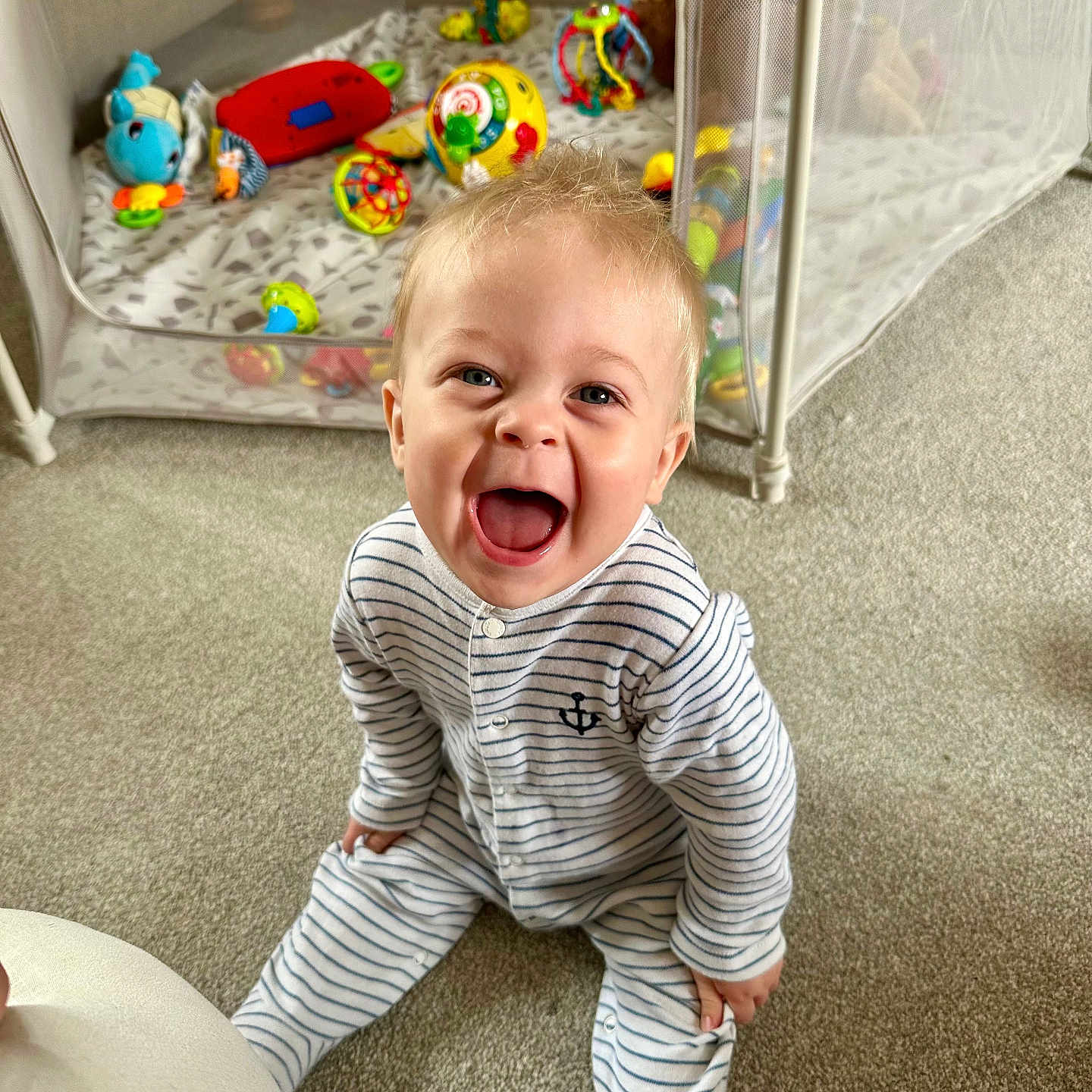 Oliver joined the competition — help win amazing prizes! baby, carpet, child, colorful, cute, expression, face, happy, home, indoor, infant, joy, laughing, person, playpen, playtime, sitting, smiling, striped_onesie, toys