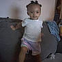 child, indoor, couch, person, hair, white_shirt, shorts, toy, blanket, wall_art, furniture, home, living_room, young_child, curious, standing, casual_clothing, dim_light, portrait, smiling