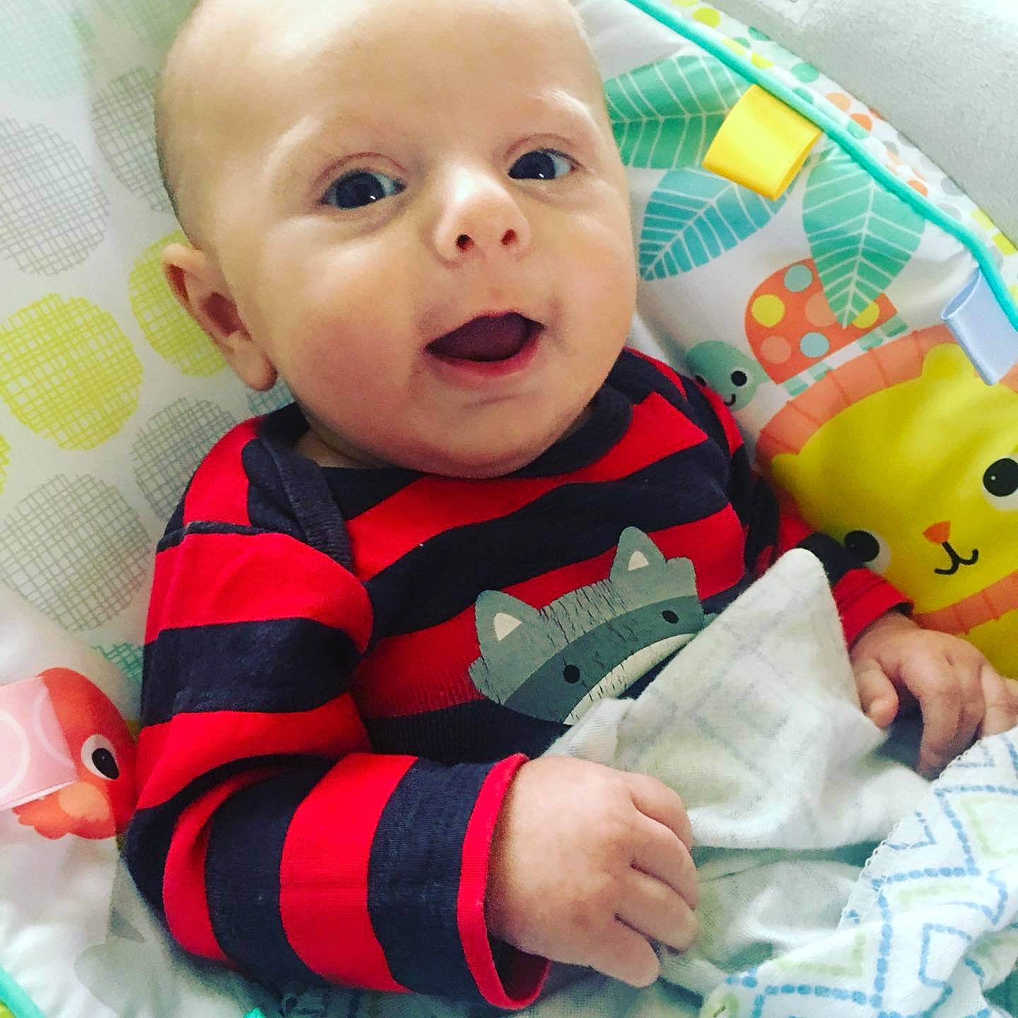 Milo is registered to the contest to win money with this photo: baby, cheek, child, eye, face, facial_expression, head, lip, mouth, nose, outerwear, person, play, product, skin, smile, textile, toddler, toy, tummy_time