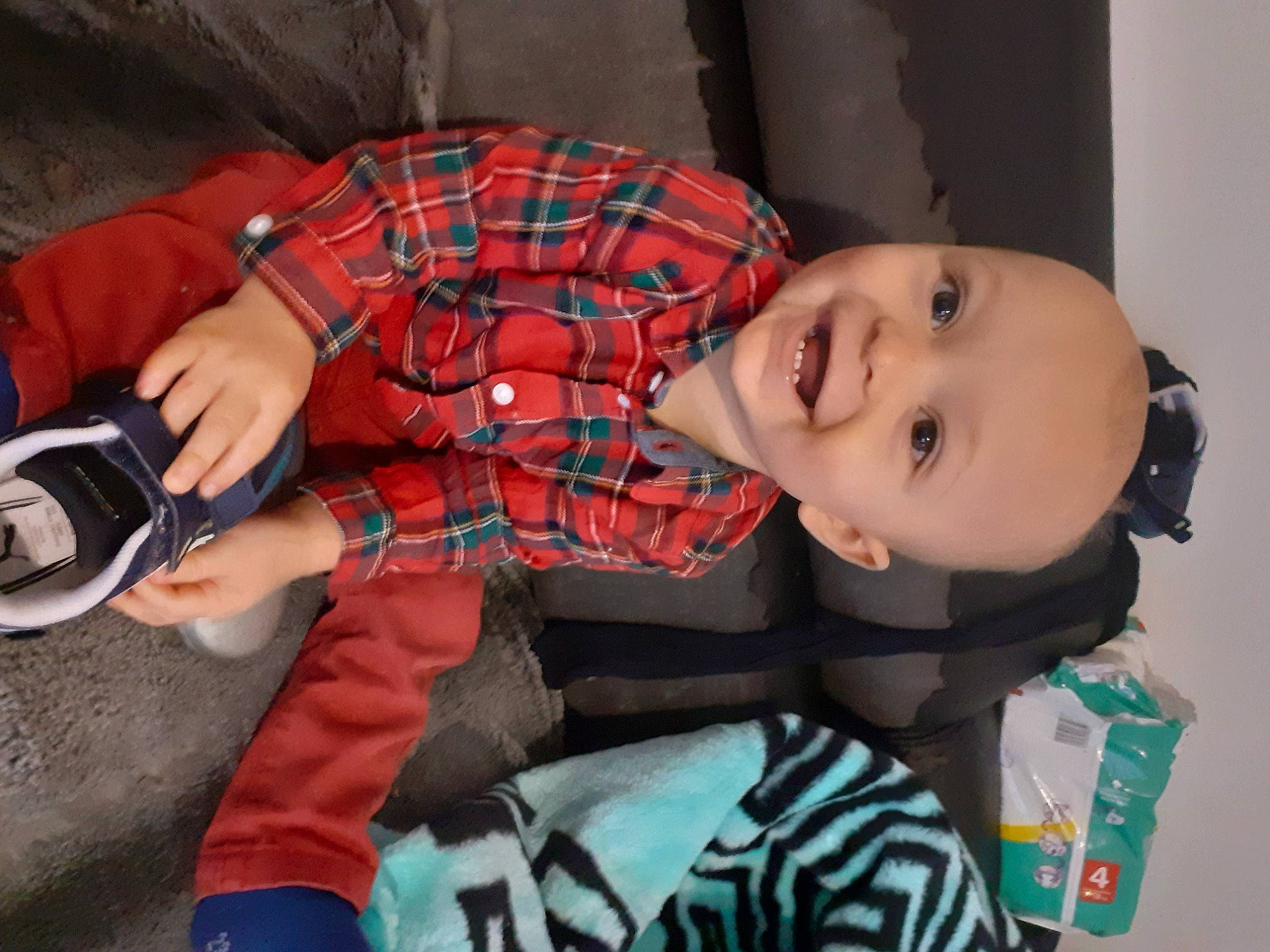 John a rejoint le concours — aidez-le/la à gagner de superbes lots ! baby, baby_toddler_clothing, carmine, child, eyewear, fun, happy, head, human_leg, joy, mouth, pattern, person, personal_protective_equipment, plaid, room, sitting, smile, sock, tartan