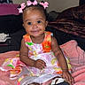 Kehlani joined the competition — help win amazing prizes! baby, child, pink_bow, dress, smile, indoor, blanket, sitting, footwear, happy, face, person, cute, infant, hair_bow, colorful_clothing, soft_texture, portrait, young_child, cozy