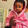 baby, child, person, pink_robe, curly_hair, hood, bathroom, towel, hand, earring, portrait, indoor, cute, expression, adult_hand, wall_art, mirror, skin, clothing, young