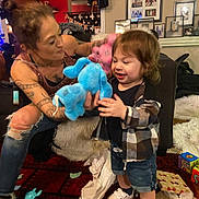 Micah joined the competition — help win amazing prizes! toddler, child, adult, woman, tattoos, stuffed_animal, blue_toy, pink_toy, living_room, carpet, toys, clothing, shorts, sneakers, smile, playful, furniture, photographs, home_interior, interaction