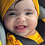 baby, child, smiling, yellow_turban, yellow_clothing, car_seat, safety_belt, closeup, face, cute, happy, infant, portrait, indoors, person, seatbelt, headwear, bright_colors, cheerful, small_child