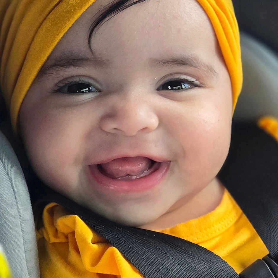 Allison is registered to the contest to win money with this photo: baby, bright_colors, car_seat, cheerful, child, closeup, cute, face, happy, headwear, indoors, infant, person, portrait, safety_belt, seatbelt, small_child, smiling, yellow_clothing, yellow_turban