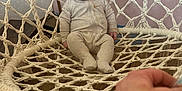 Maverick joined the competition — help win amazing prizes! baby, child, onesie, hammock, woven_chair, indoor, wooden_floor, hand, person, face, expression, curious, seated, cozy, fabric, room, wall, soft_lighting, relaxing, casual