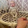 baby, casual, child, cozy, curious, expression, fabric, face, hammock, hand, indoor, onesie, person, relaxing, room, seated, soft_lighting, wall, wooden_floor, woven_chair