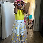 Laysha a rejoint le concours — aidez-le/la à gagner de superbes lots ! bracelet, child, cute, doorway, fashion, floral_skirt, footwear, happy, indoor, person, pink_hat, portrait, sandals, smiling, standing, sun_hat, sunglasses, toy, wooden_floor, yellow_top