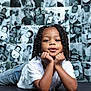 artistic, baby_photos, black_background, braided_hair, child, confident, cute, face, hands, indoor, jeans, lying_down, necklace, photo_collage, portrait, relaxed, smile, studio, white_shirt, young