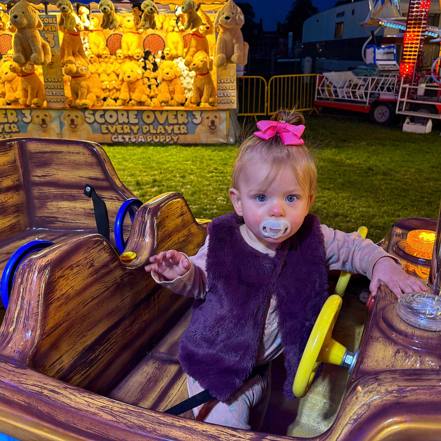 Talia-Rose is registered to the contest to win money with this photo: amusement_park, bow, carnival, child, fun, game_booth, grass, night, outdoor, pacifier, person, play, plush_toys, prizes, ride, steering_wheel, toddler, toy, vest, wood