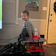 Bentlee joined the competition — help win amazing prizes! blanket, boy, carpet, casual_clothing, child, door, furniture, indoor, light_switch, living_room, play_dough, play_kitchen, poster, smile, stool, television, toy, wall, window, wreath