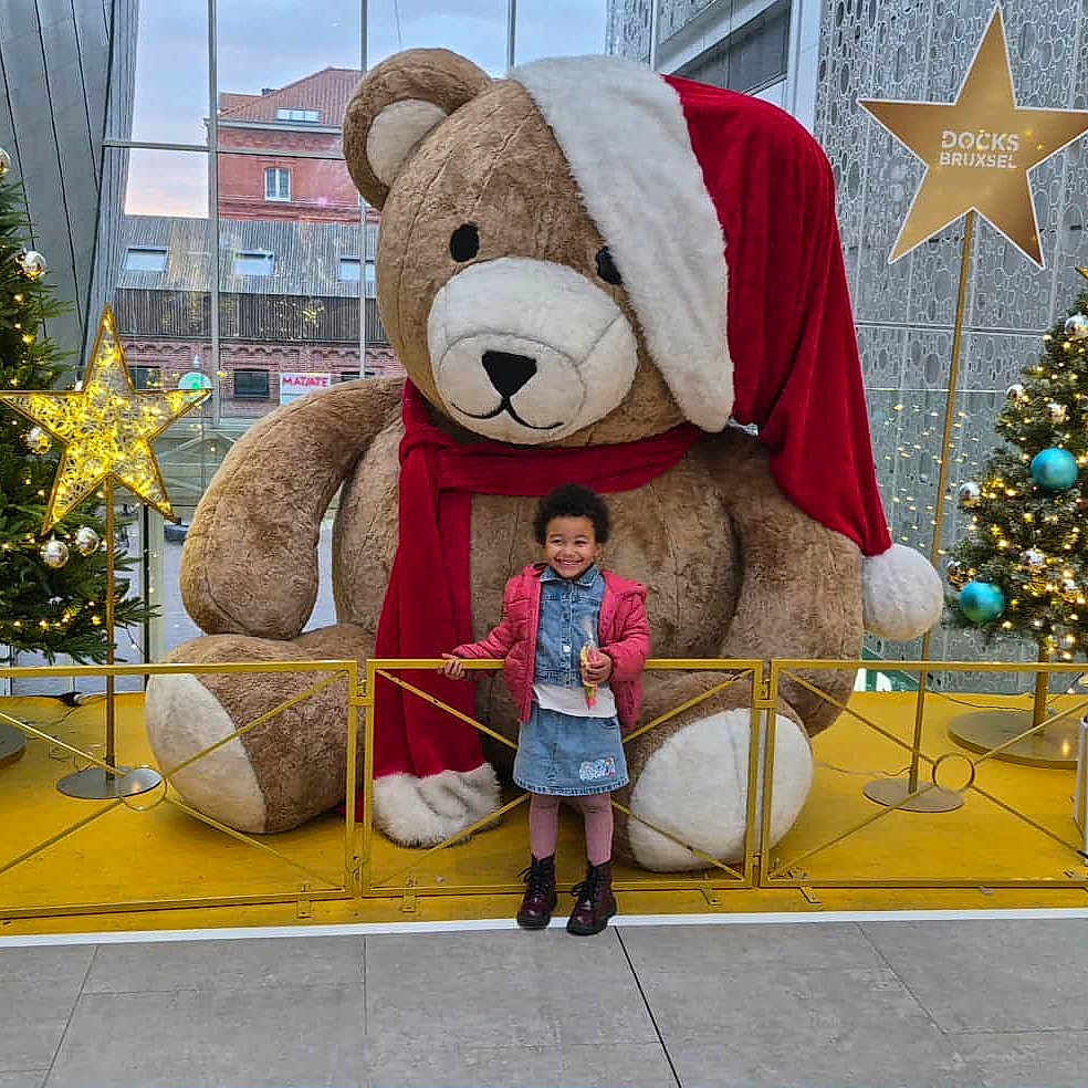 Maelys Maes Leonard participe au concours pour gagner de l'argent avec cette photo : celebration, child, christmas_tree, decorations, festive, floor_tiles, gift_box, glass_ceiling, happy, holiday_decor, indoor, lights, metal_railing, modern_architecture, posing, santa_hat, scarf, smiling, teddy_bear, winter_clothing