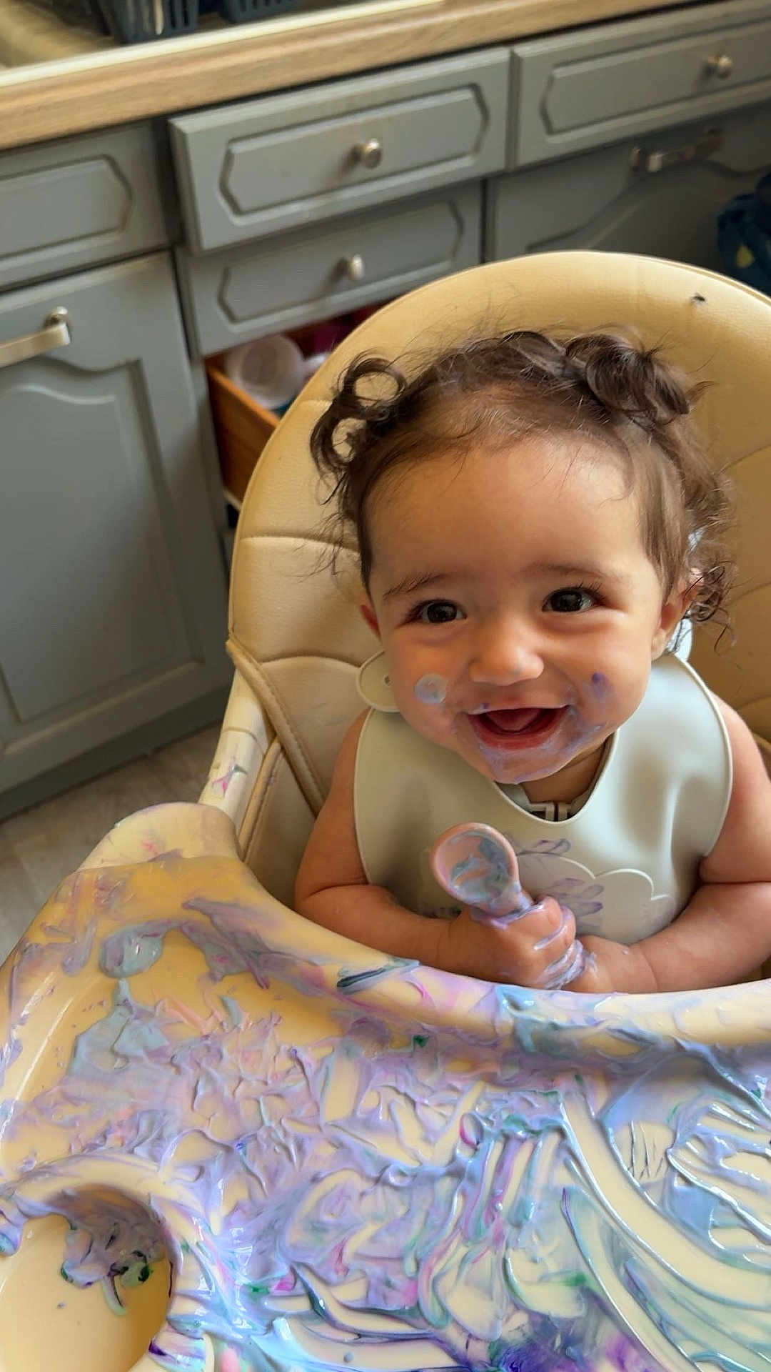 Layna participe au concours pour gagner de l'argent avec cette photo : toddler, high_chair, messy, food, spoon, smiling, curly_hair, kitchen, baby, face_paint, happy, colorful, child, feeding, playful, cute, indoor, bib, table, expression