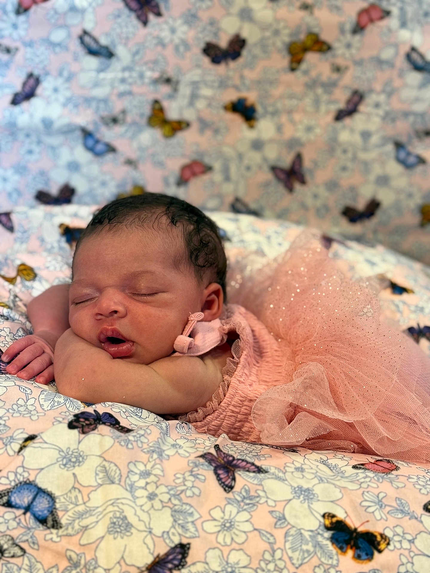 Amani joined the competition — help win amazing prizes! baby, newborn, sleeping, pink_dress, tulle, blanket, butterfly_pattern, floral_pattern, soft_texture, infant, cute, peaceful, resting, portrait, indoors, cozy, delicate, child, toddler, head