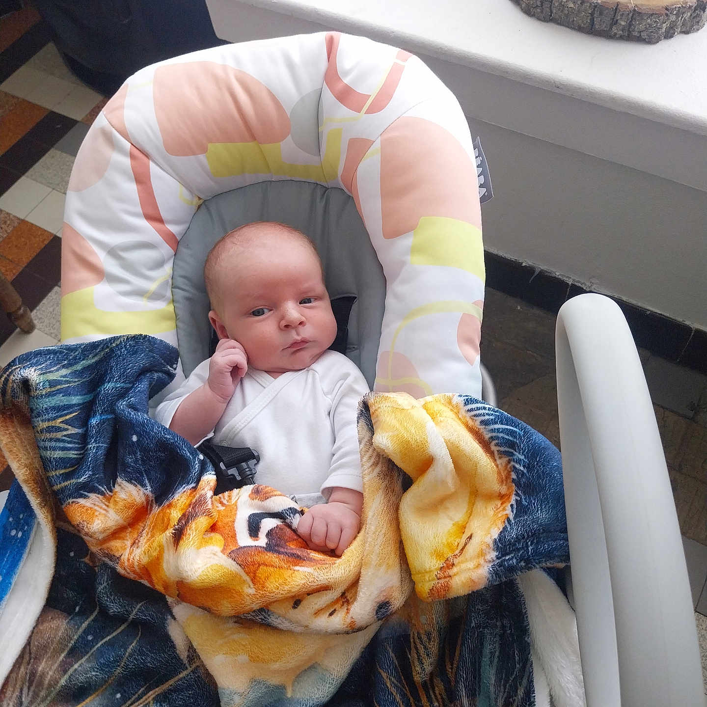 Jules a rejoint le concours — aidez-le/la à gagner de superbes lots ! baby, baby_seat, blanket, blanket_pattern, clothing, colorful, cup, curious, expression, face, floor_tiles, furniture, hand, head, indoor, person, seatbelt, sitting, table, wood_coaster