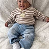 baby, child, smiling, portrait, indoor, blanket, beanie, sweater, striped_clothing, jeans, sneakers, necklace, fashion, sitting, lying_down, happy, face, infant, cozy, furry_blanket