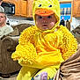 Bea joined the competition — help win amazing prizes! baby, child, costume, yellow, duck, plush, indoors, living_room, person, face, cute, sitting, clothing, hood, orange, furniture, home, people, carpet, couch