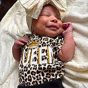 Miloni is registered to the contest to win money with this photo: baby, newborn, smiling, headband, bow, leopard_print, clothing, blanket, infant, cute, sleepy, soft_texture, closeup, portrait, resting, small_hands, cozy, happy, child, adorable