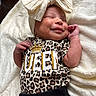 baby, newborn, smiling, headband, bow, leopard_print, clothing, blanket, infant, cute, sleepy, soft_texture, closeup, portrait, resting, small_hands, cozy, happy, child, adorable