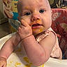 Evelynn joined the competition — help win amazing prizes! baby, infant, child, high_chair, portrait, face, eyes, smiling, sitting, feeding, baby_food, puree, messy, hand, finger, pink_clothing, bib, tray, indoor, colorful_background