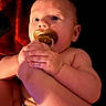 Evelynn is registered to the contest to win money with this photo: baby, infant, child, portrait, pacifier, sucking_pacifier, close_up, face, eyes, hands, fingers, bare_arms, sitting, indoor, warm_lighting, red_background, dark_background, curious, photograph, portrait_orientation