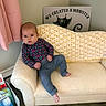 baby, child, couch, blanket, crochet, clothing, pants, long_sleeve, face, person, indoor, floor, wood_floor, basket, books, sign, curtain, wall, foot, sitting