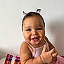 baby, child, smiling, face, pigtails, pink_clothing, blanket, plaid, happy, cute, infant, portrait, skin, hand, fingers, sitting, indoors, wall, cozy, toddler