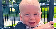 Atlas joined the competition — help win amazing prizes! baby, child, daylight, face, fence, grass, grinning, happy, infant, outdoor, park, play_equipment, playground, portrait, safety_bar, seated, smiling, sunlight, swing, trees