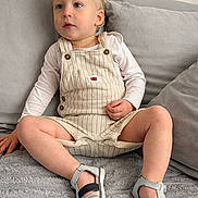 Neylan participe au concours pour gagner de l'argent avec cette photo : toddler, child, blonde_hair, overalls, sandals, long_sleeve_shirt, couch, gray_couch, indoor, sitting, curious, young_child, casual_clothing, footwear, comfortable, relaxed, home_interior, furniture, portrait, person