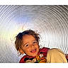 bright, candid, casual_clothing, child, colorful, curly_hair, expression, face, fun, happy, indoor, joy, light, metallic, playful, portrait, smiling, spiral, tunnel, young_child