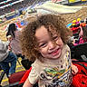 Andres is registered to the contest to win money with this photo: child, curly_hair, smile, tshirt, monster_jam, stadium, event, spectators, seats, monster_truck, dirt_track, crowd, red_jacket, happy, indoor, person, casual_clothing, fun, family_outing, entertainment