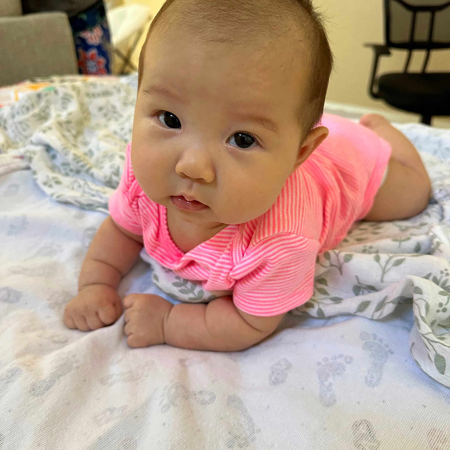 Allison is registered to the contest to win money with this photo: baby, blanket, child, chubby_cheeks, closeup, curious, cute, expression, face, footprint_pattern, home, indoor, infant, laying_down, person, pink_clothing, resting, soft_texture, tummy_time, young_child