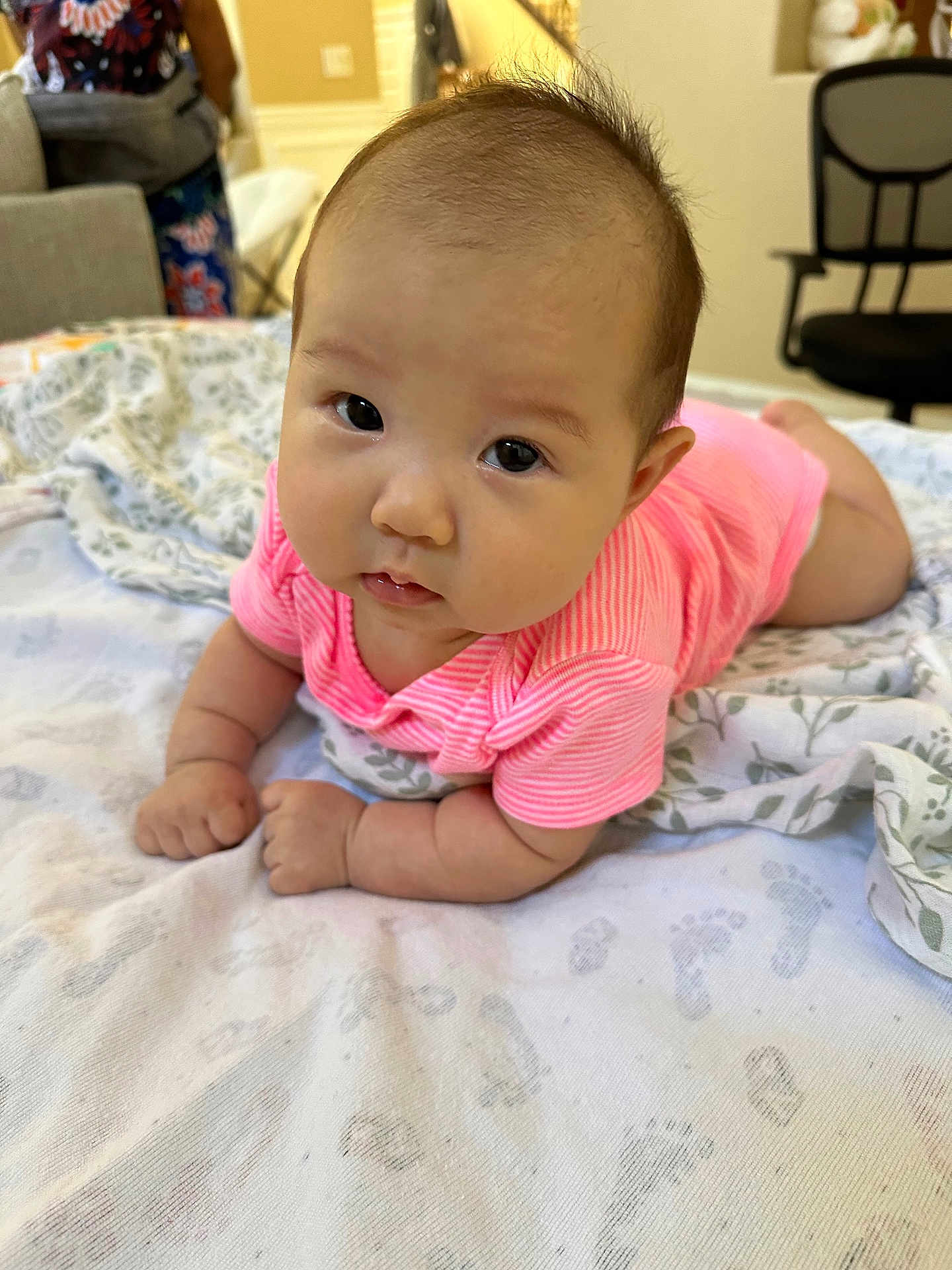 Allison is registered to the contest to win money with this photo: baby, infant, pink_clothing, tummy_time, blanket, footprint_pattern, indoor, person, face, cute, child, curious, resting, soft_texture, home, young_child, chubby_cheeks, expression, laying_down, closeup