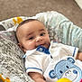 Ram is registered to the contest to win money with this photo: baby, infant, cushion, elephant_print, white_shirt, blue_bear_patch, smile, curious, indoor, carpet, toy, colorful, portrait, child, cute, soft_lighting, relaxed, seated, closeup, happy
