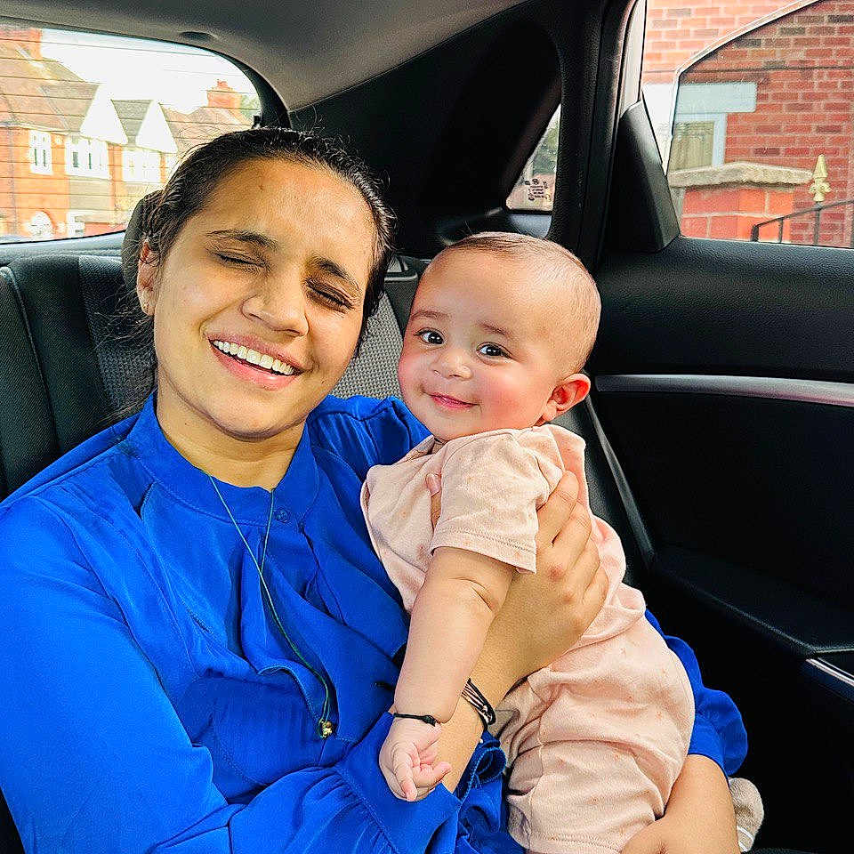 Ram is registered to the contest to win money with this photo: affection, baby, blue_clothing, car_interior, casual, child, daylight, family, hand, happy, holding, person, pink_clothing, portrait, seat, skin, smile, urban_background, window, woman