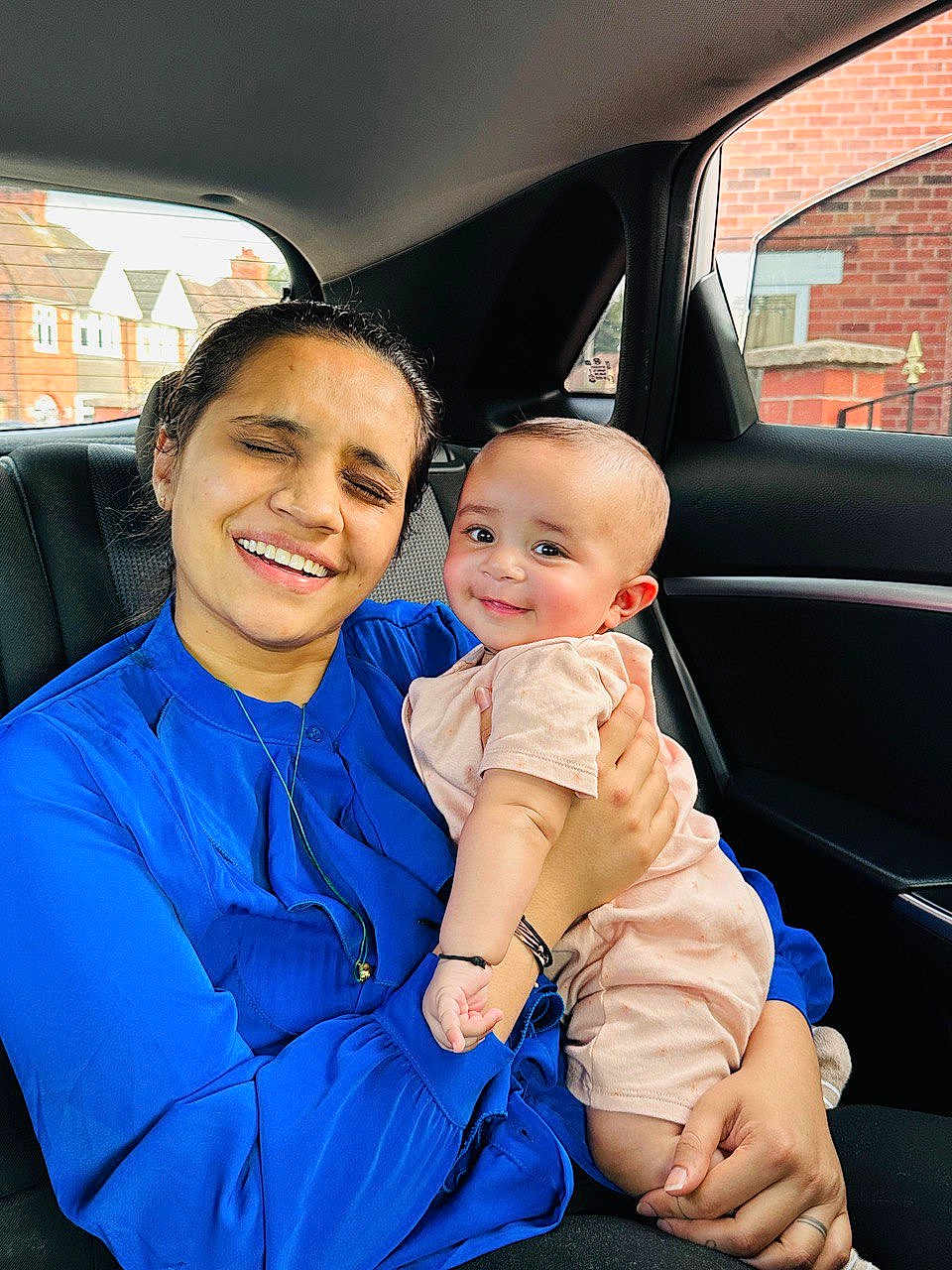 Ram is registered to the contest to win money with this photo: woman, baby, child, car_interior, blue_clothing, pink_clothing, smile, happy, portrait, holding, seat, window, urban_background, family, affection, person, casual, daylight, skin, hand
